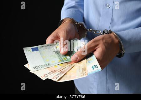 Korruption. Mann in Handschellen, der Euro-Banknoten auf schwarzem Hintergrund hält, Nahaufnahme Stockfoto