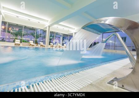 Geräumiges Hallenbad mit Whirlpool, Wasserkaskade und entspannenden Liegestühlen in einem hellen, modernen Wellnessresort Stockfoto
