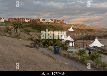 Ein malerischer Blick auf Barry Island, Wales, mit der Promenade mit ihren berühmten weißen Baumkronen und farbenfrohen Strandhütten. Die Leute schlendern am Strand entlang Stockfoto