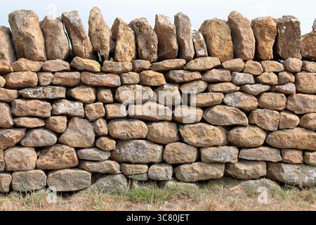 Nahaufnahme einer traditionellen Dorset Trockensteinmauer aus Portland-Stein mit großen stehenden Steinen in der Ummantelung, Gras vor und das Meer dahinter. Stockfoto