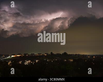 Ein mächtiger Blitz beleuchtet die dramatischen Sturmwolken und ein entferntes Viertel in Pennsylvania bei Nacht. Stockfoto