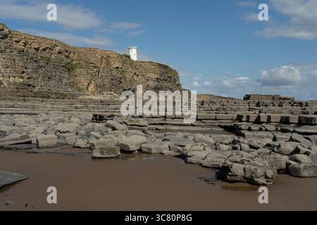 Ebbe offenbart den felsigen Strand in Nash Point, Wales, mit seinem berühmten Leuchtturm auf den Klippen, der Schiffe durch den Bristol Channel führt. Stockfoto