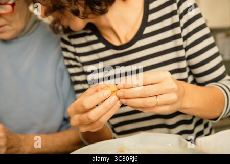 Nahaufnahme einer Seniorin und einer mittelgroßen Frau, die nebeneinander in einer Küche stehen und Kekse machen Stockfoto