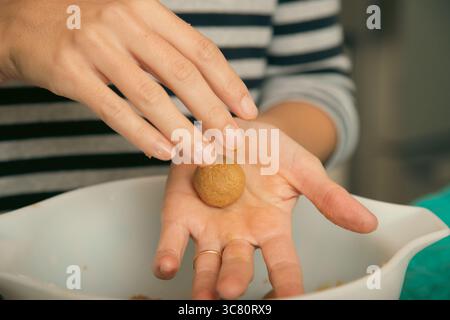 Nahaufnahme einer mittelerwachsenen Frau, die in einer Küche steht und Kugeln Keksenteig in der Hand rollte Stockfoto