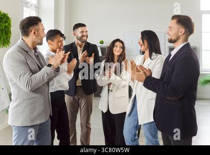 Gruppe von multiethnischen glücklichen Geschäftsleuten, Männer und Frauen, die im Kreis stehen und applaudieren. Stockfoto