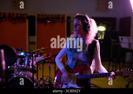 Rote E-Gitarre, die auf dem Stand im Studio sitzt, mit orangefarbenen Paneelen und lila-gelben Lichtern Stockfoto