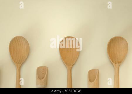 Natürliche Holzlöffel und -Schaufeln auf beigefarbenem Hintergrund. Rustikale, umweltfreundliche Küchenutensilien zum Kochen, Backen und Servieren. Stockfoto