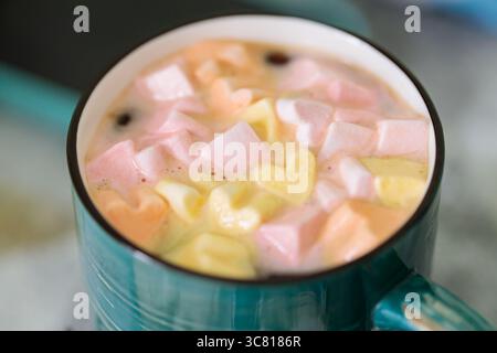 Heiße Schokolade mit bunten Marshmallows in türkisfarbenem Becher, gemütliches Wintergetränk Stockfoto
