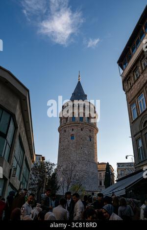 Ein Niedrigwinkelfoto des Galatenturms in Istanbul, Türkei, mit einer Menge Menschen, die sich an der Basis versammelten, wahrscheinlich Touristen, die das historische Wahrzeichen besuchen. Stockfoto