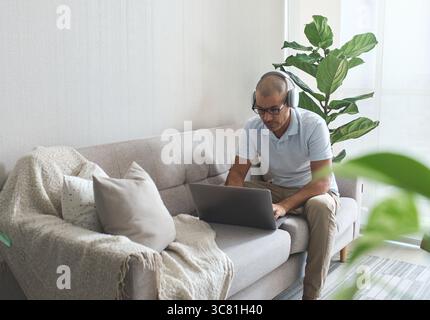 Fokussierter Mitarbeiter, der von zu Hause aus mit Laptop und Kopfhörern arbeitet Stockfoto
