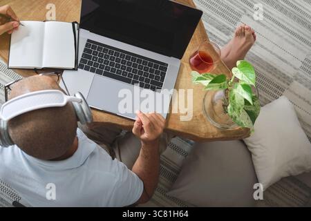 Draufsicht auf Freelancer, die Kopfhörer tragen, von zu Hause aus am Laptop arbeiten, Musik hören und Tee trinken Stockfoto