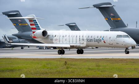 Ein Regionalflugzeug mit amerikanischer Eagle-Lackierung fährt auf einer Start- und Landebahn. Im Hintergrund sind mehrere große militärische Transportflugzeuge parat Stockfoto