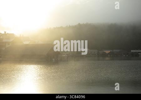 Mystischer Vormittag am Königssee in Schönau mit Bootshäusern. Sonnenaufgang und wunderschöne Nebelschwaden über dem Königssee im Becken Stockfoto
