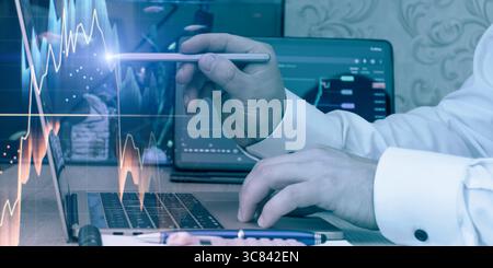 Geschäftsmann zeigt auf einem Notebook auf digitale Finanzdiagramme und interpretiert Datentrends für Investitionsentscheidungen in einem modernen Arbeitsbereich. Stockfoto
