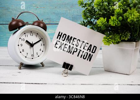 Text für die Befreiung von der Wohnung auf Papierkarte mit Wecker auf hölzernem Hintergrund geschrieben Stockfoto