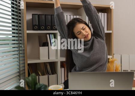 Frau dehnt sich aus und arbeitet zu Hause, schöne Frau entspannt sich am Schreibtisch, dehnt und ruht im Home Office, Ruhe und Profil des Arbeiters für Selbstpflege, Stockfoto