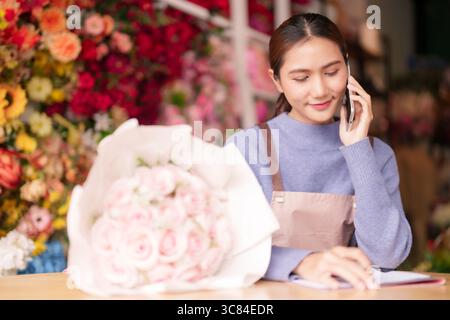 Erwachsene asiatische Frau arbeitet Blumengeschäft nimmt Telefonbestellungen verwaltet Geschäft Arrangieren schöne frische Blumen Kundenservice Interaktion. Stockfoto