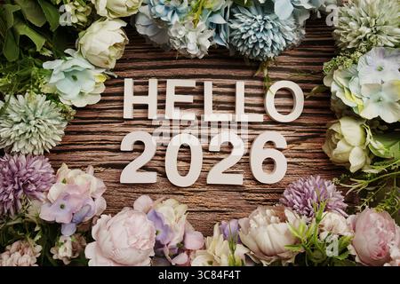 Hallo 2026 Buchstaben mit Blumen auf hölzernem Hintergrund Stockfoto
