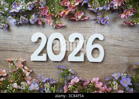 2026 Jahre Zahl mit Blumenrahmen von oben auf hölzernem Hintergrund. Hallo, Willkommen und Goodbye Neujahrskonzept Stockfoto