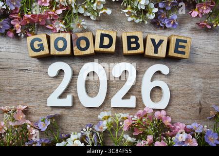 Auf Wiedersehen 2026 Jahre Zahl mit Blumenrahmen von oben auf hölzernem Hintergrund Stockfoto