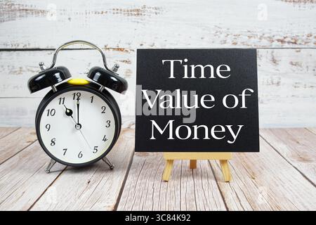 Zeitwert des Geldtextes mit Staffelei und Wecker auf hölzernem Hintergrund Stockfoto