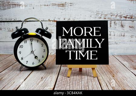 Mehr Text zur Familienzeit mit Staffelei und Wecker auf hölzernem Hintergrund Stockfoto