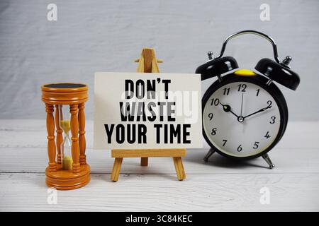 Verschwenden Sie Ihre Zeit nicht mit Sanduhr und Wecker auf hölzernem Hintergrund Stockfoto