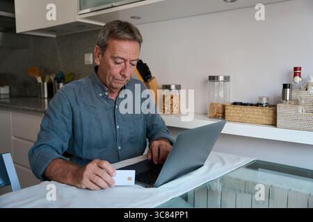 Senior Mann, der online mit Kreditkarte in der Küche bezahlt Stockfoto