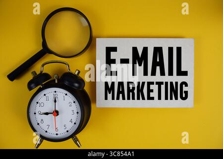 E-Mail Marketingtext auf Papier mit Lupe und Wecker auf gelbem Hintergrund Stockfoto