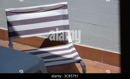 Gestreifter Lounge-Stuhl an der Außenwand bei Sonnenlicht Stockfoto