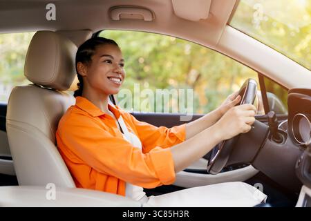 Junge afroamerikanische Frau lächelt selbstbewusst, während sie ihr Auto fährt Stockfoto