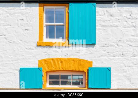Zwei rechteckige Glasfenster mit gelb bemalten Umrandungen und blauen lamellenfenstern in einem weißen, mit Wasch ummauerten Gebäude, Portpatrick, Stockfoto