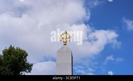 Moskau, Russland - 17. Juli 2025: Goldener russischer Doppeladler auf einem hohen Granitobelisken vor einem leuchtend blauen Himmel Stockfoto