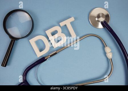 DBT-Alphabetbuchstaben der dialektischen Verhaltenstherapie mit Stethoskop und Lupe auf blauem Hintergrund Stockfoto