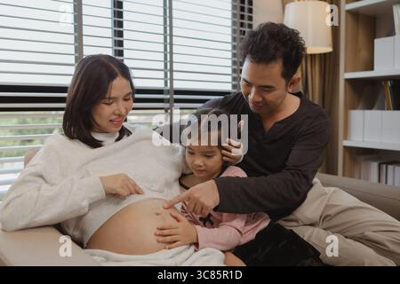 Eine schöne Familie verbringt Zeit zusammen in ihrem Haus, eine schwangere Mutter sitzt mit ihrem Mann und ihrer Tochter auf der Couch und genießt eine glückliche gemeinsame Zeit Stockfoto