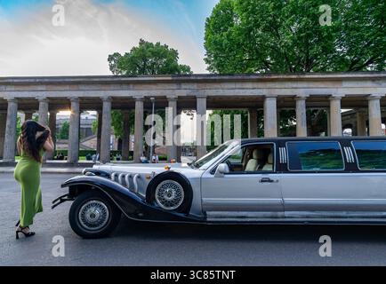 Stilvolle Frau in grünem Kleid posiert im Sommer in der Alten Nationalgalerie in der klassischen Stretchlimousine vor historischen Kolonnaden. Stockfoto
