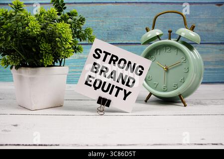 Starker Text der Marke Eigenkapital auf Papierkarte mit Wecker auf hölzernem Hintergrund geschrieben Stockfoto