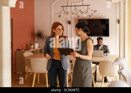 Weibliche Kollegen diskutieren Online-Daten über ein digitales Tablet, während sie gemeinsam im Büro stehen Stockfoto