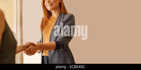 Mittelteil der Geschäftsfrau, die dem Partner Handschlag gibt und gleichzeitig einen erfolgreichen Geschäftsvertrag gegen die Wand im Büro versiegelt Stockfoto