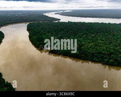 Aus der Vogelperspektive auf den schlammigen Fluss, der sich durch einen dichten, grünen Regenwald unter einem bewölkten Himmel schlängelt, in Bani Town, Rivers State. Stockfoto
