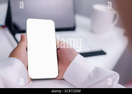 Handheld-Smartphone mit leerem weißen Bildschirm in einem modernen Arbeitsbereich, perfekt für die Präsentation mobiler Apps, Websites oder Marketinginhalte Stockfoto