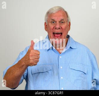 Ein älterer Mann trägt ein blau-weißes kariertes Hemd mit einer Geste nach oben und einem Hochgefühl im Gesicht Stockfoto