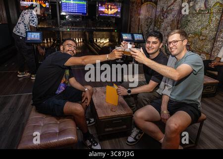 Gruppe junger Männer, die in einer Bowlingbahn Biergläser anstoßen, feiern und einen Abend mit Getränken, Spaß und Kameradschaft genießen. Stockfoto