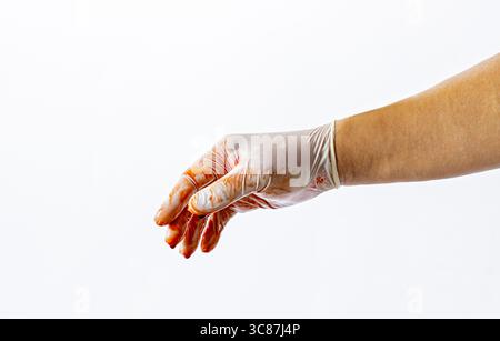 Eine Hand mit Handschuhen, die mit roter Flüssigkeit, möglicherweise Blut, bedeckt ist, wird vor weißem Hintergrund verlängert, was auf einen medizinischen oder forensischen Kontext hindeutet Stockfoto