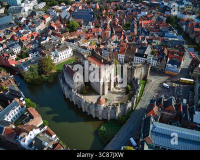 Die robusten Steinmauern des Schlosses Gravensteen aus der Vogelperspektive umgeben das ruhige Wasser und bilden einen Kontrast zu den leuchtenden roten Dächern der umliegenden Stadt Gent, Flandern, Belgien. Stockfoto