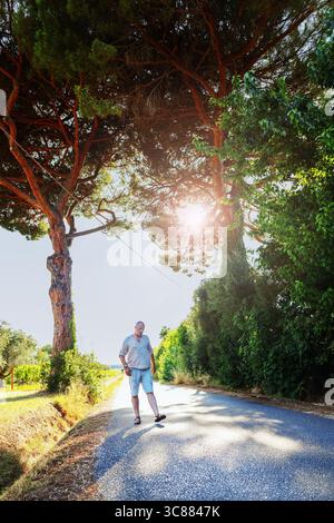 Ruhiger Reisemoment auf einer sonnigen Straße in der Toskana, Mann, der die Landschaft im warmen Abendlicht erkundet. Stockfoto