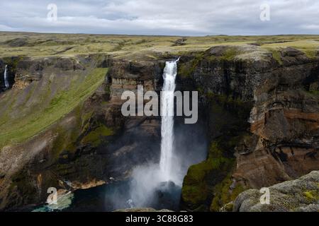Der Haifoss Wasserfall stürzt von hohen Klippen in einen ruhigen Pool, umgeben von üppigem Grün und dramatischen Felsformationen. Diese atemberaubende Aussicht fängt die Schönheit der isländischen Naturwunder ein. Stockfoto