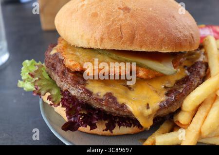 Köstlicher Cheeseburger mit Pommes frites auf einem Teller. Nahaufnahme eines Cheeseburgers mit erfinderischen Belägen auf einem Teller, serviert neben goldenem Französisch Stockfoto