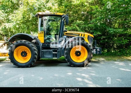 Gelb-schwarzer JCB Fastrac-Traktor, der an sonnigen Tagen neben Waldbäumen geparkt wird, große Räder und moderne Landmaschinen. Stockfoto