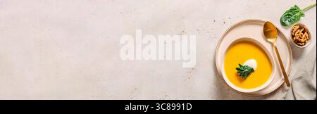Kürbiscremesuppe serviert Spinat, Nüsse, Sauerrahm. Banner. Leckerer hausgemachter Kürbis, süße Kartoffel oder Karottensuppe in der Schüssel auf neutralem Pastelhintergrund. Stockfoto
